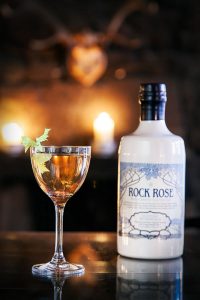 Bottle of Rock Rose Gin and Huntsman Cocktail served in a vintage glass and garnished with celery leaf