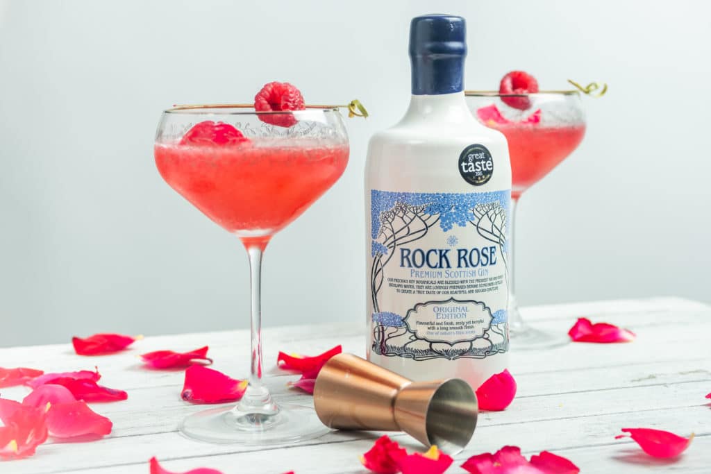 Bottle of Rock Rose Gin and Happy 6th Fizz cocktail served in two coupe glass and garnished with raspberry