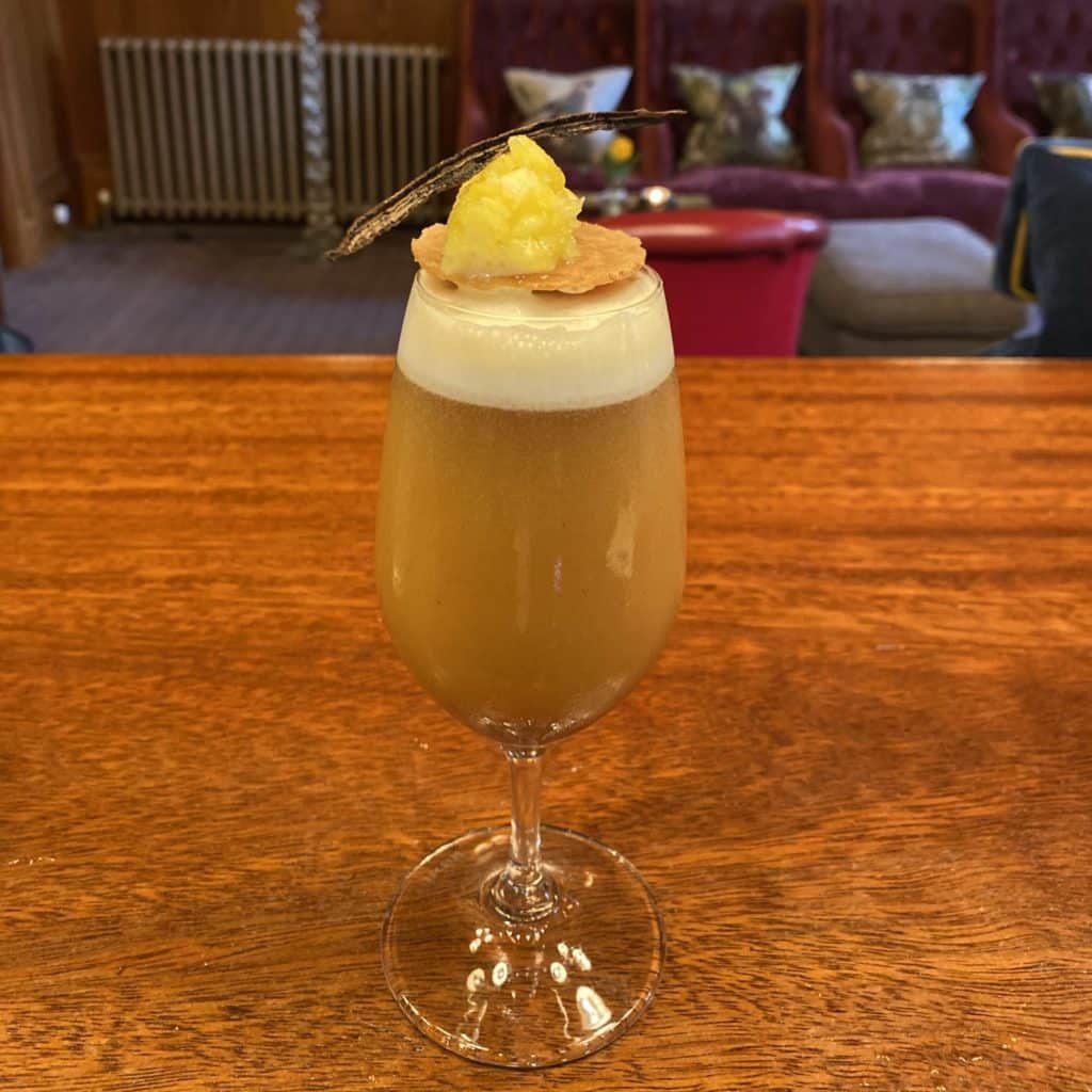 Gingerbread and Gin cocktail served in a flute glass and garnished with a thin biscuit, pineapple brunoises and vanilla pod