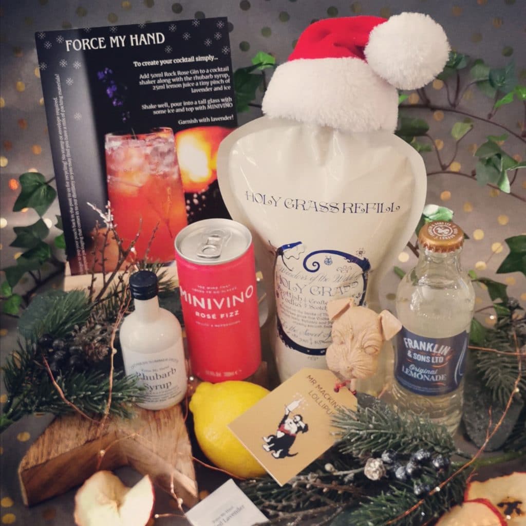 Content of the Refill Rewards Club box for December 2020 including Holy Grass Vodka pouch wearing a Santa's hat, can of rosé fizz, rhubarb syrup, lemonade and a Mr Mackintosh Lollipup