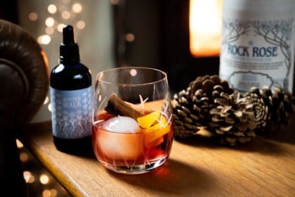 Bottle of Rock Rose Gin winter edition and Winter Walk liquid garnish with Winter Negroni Cocktail served with ice ball and garnished with orange peel and cinnamon stick