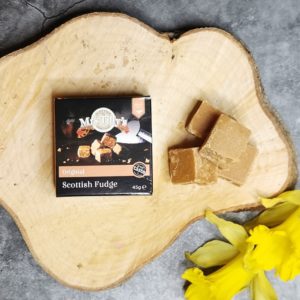 Box of Mrs Tillys Fudge on a slice of tree stump and daffodils