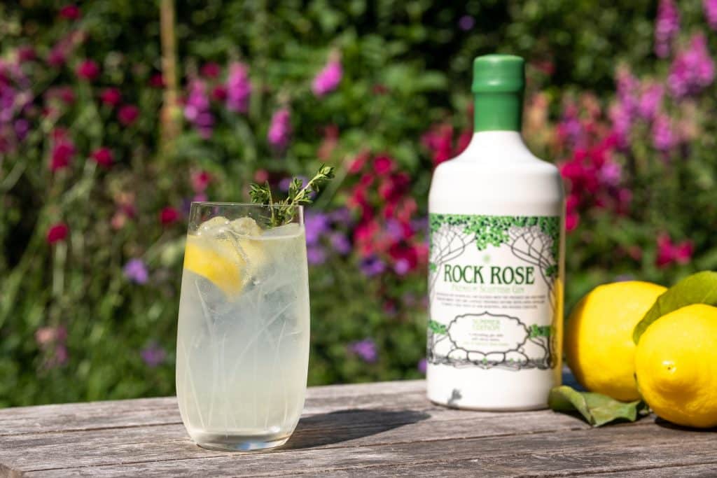 Bottle of Rock Rose Gin summer edition and Lemon Thyme Collins cocktail served in a tall glass