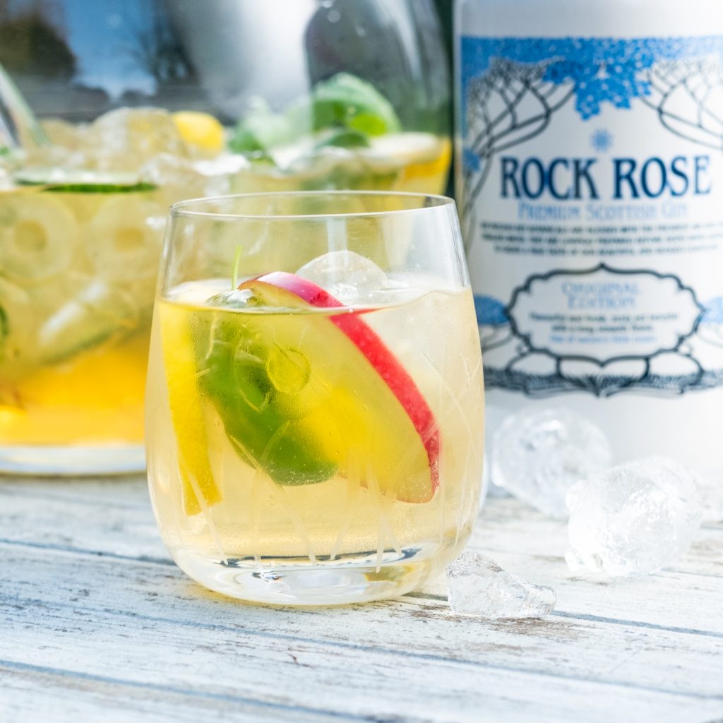 Bottle of Rock Rose Gin and Gin & Elderflower Punch served in a glass and garnished with slices of apple, cucumber and basil leaves