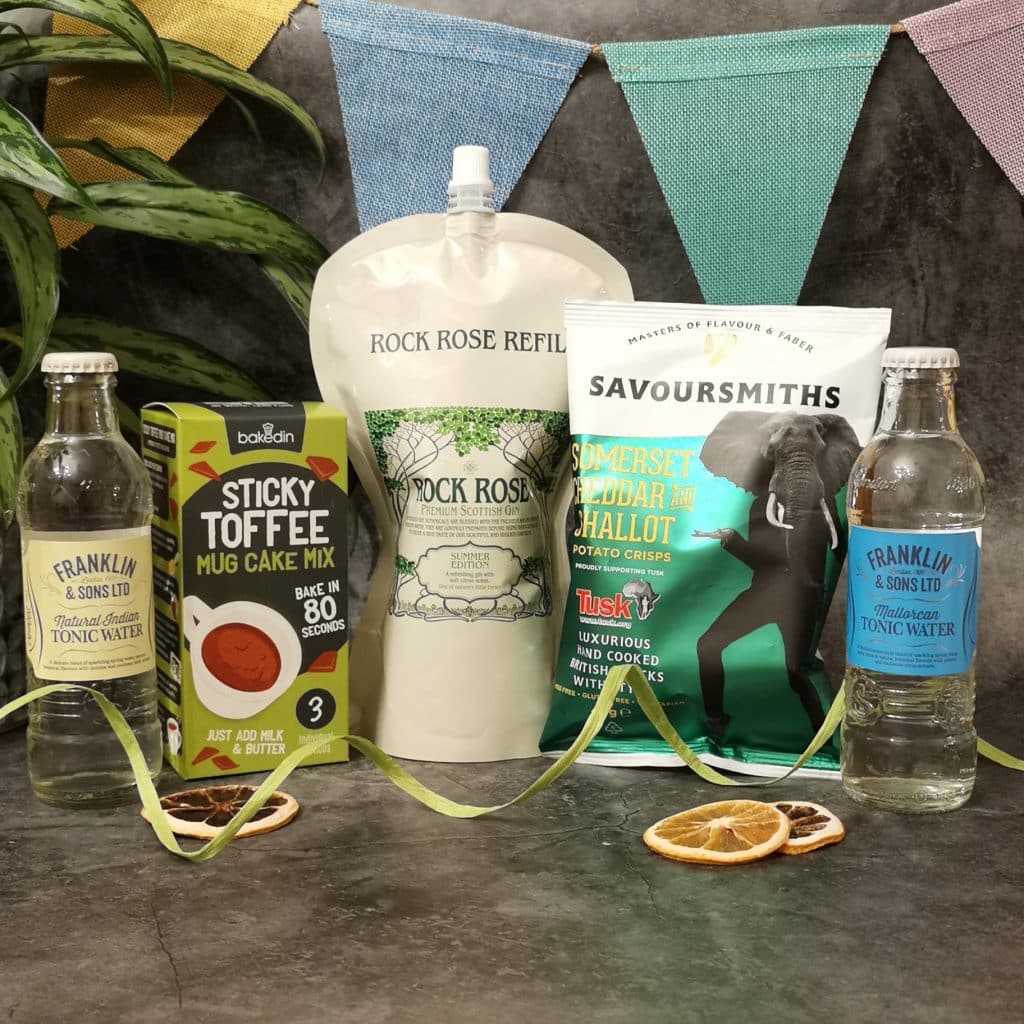 Content of the Refill Rewards Club box for August 2021 including Rock Rose Gin pouch, tonic waters, cheddar and shallot crisps and sticky toffee mug cake mix