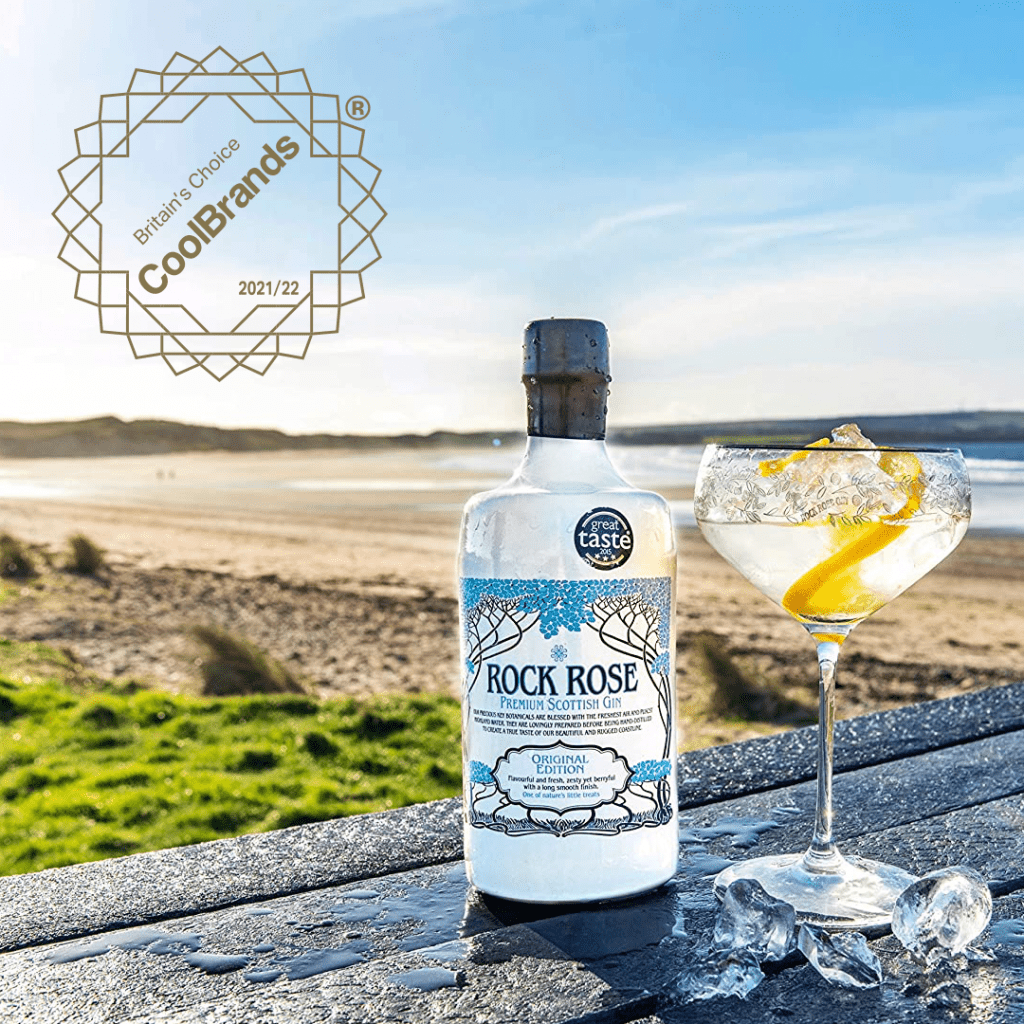 Featured image for Britain's Choice CoolBrands 2021-22 award with bottle of Rock Rose Gin and cocktail on a picnic table on the beach