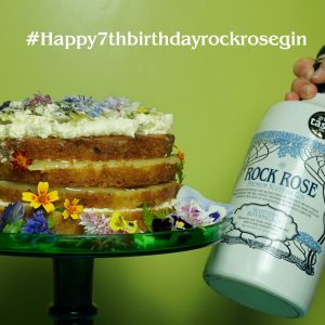 Featured image to celebrate Rock Rose Gin 7th Birthday with a birthday cake and a bottle of Rock Rose Gin