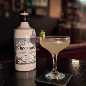 Bottle of Rock Rose Gin with From Under A Rock cocktail - by Joshua Bishop - served in a coupe glass and garnished with lime