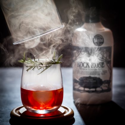 Bottle of Rock Rose Gin Navy Strength with Rosemary Smoked Negroni cocktail smoked under a cloche with flamed rosemary