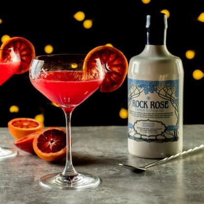 Bottle of Rock Rose Gin and Blood Orange Fizz cocktail served in a coupe glass and garnished with a slice of blood orange
