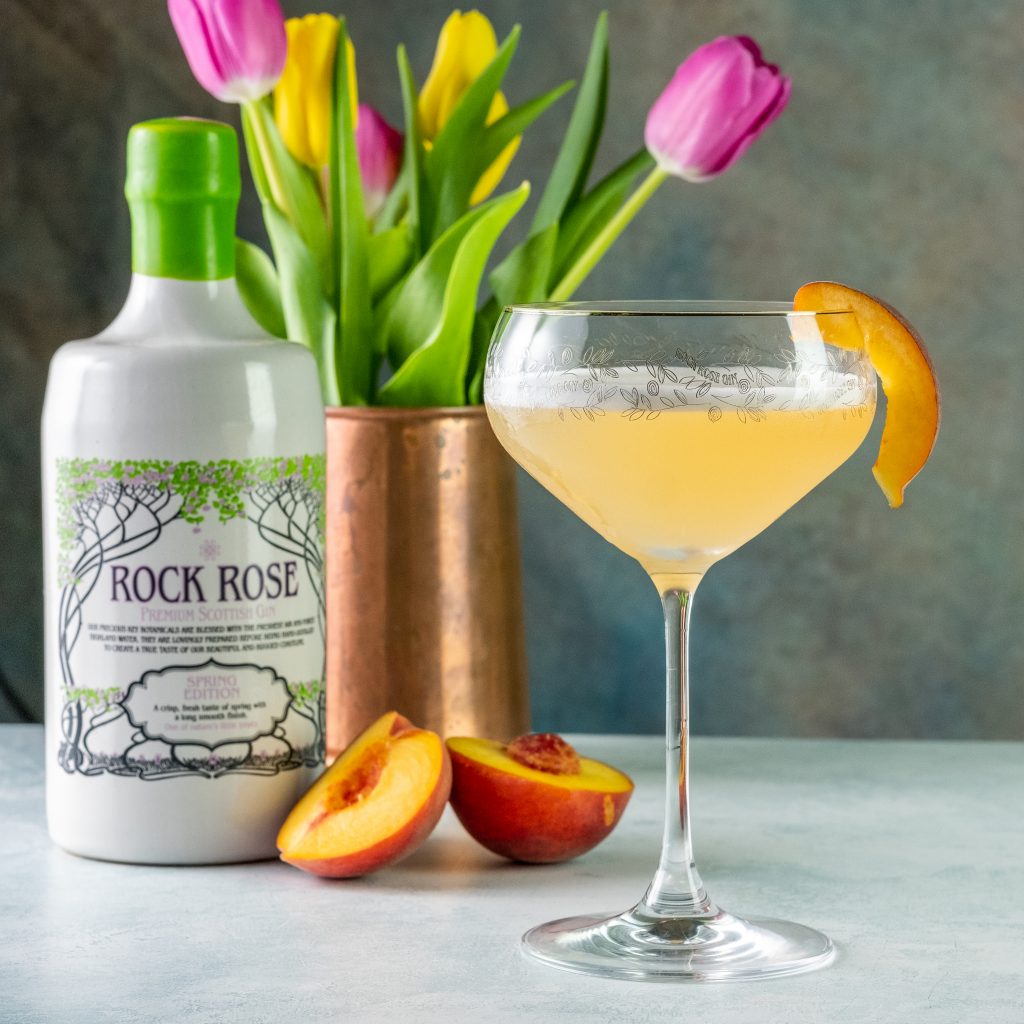 Bottle of Rock Rose Gin Spring Edition and The Perfect Lady cocktail served in a coupe glass and garnished with a slice of peach