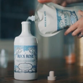 Hands emptying a refill pouch in a Rock Rose Gin ceramic bottle