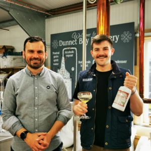 Martin and Craig in the still house displaying a bottle of Rock Rose Gin Smoked Orange and a cocktail in a coupe glass