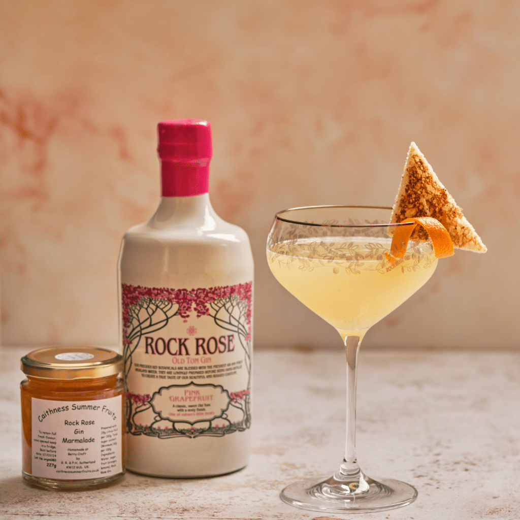 Breakfast Martini served in a cocktail glass garnished with a triangle of melba toast and orange peel next to a Rock Rose Pink Grapefruit Old Tom Gin bottle and Rock Rose Gin Marmalade jar