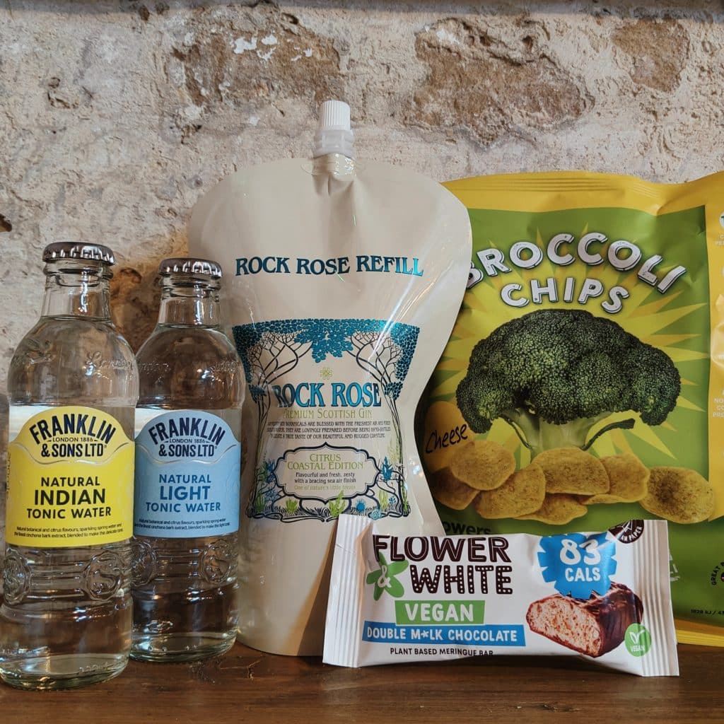 Content of the Refill Rewards Club box for January 2023 including Rock Rose Gin Citrus Coastal edition pouch, 2 tonic waters, 1 pack of Broccoli chips and 1 vegan chocolate bar