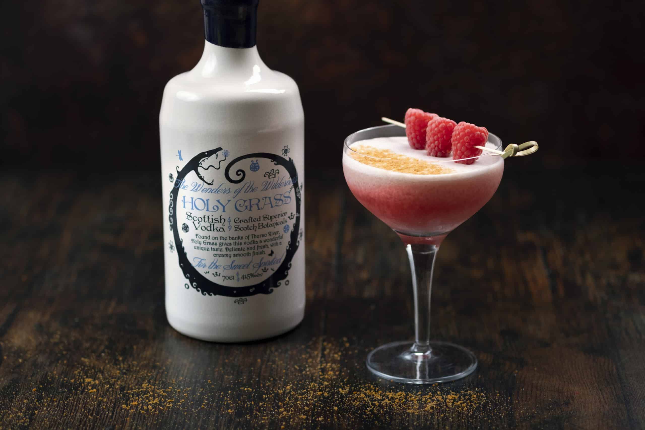 Bottle of Holy Grass Vodka and Caithness Cranachan cocktail served in a coupe glass and garnished with finely grated Lotus Speculoos biscuit and skewered raspberries